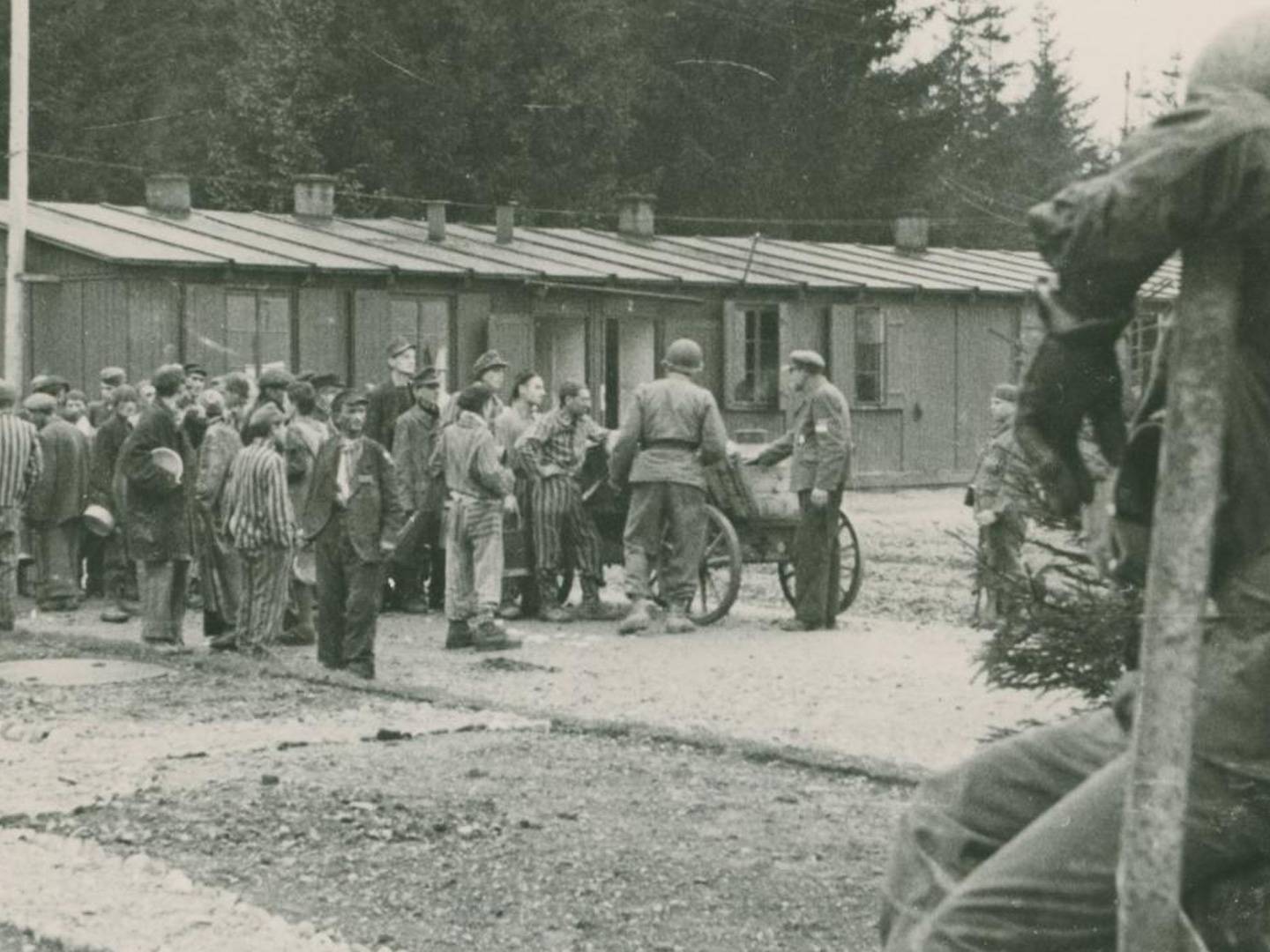 US-amerikanische Soldaten und befreite KZ-Häftlinge vor SS-Baracken am Lager Kaufering I.